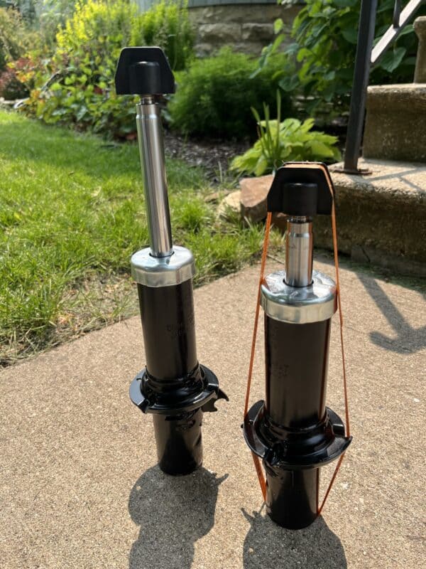 Shock absorbers on a concrete patio with greenery in the background, designed for car suspension upgrades, showcasing high-performance automotive parts for enhanced handling and ride quality.