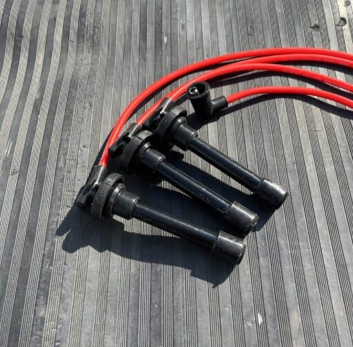 High-performance ignition wires with black boots and red wires, designed for car engine optimization, laid on a textured black surface. Perfect for improving engine spark and performance.