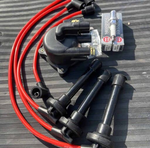 Spark plug wires, ignition coil, distributor cap, and spark plug, automotive ignition system components used for vehicle performance and maintenance, photographed on a black textured surface.