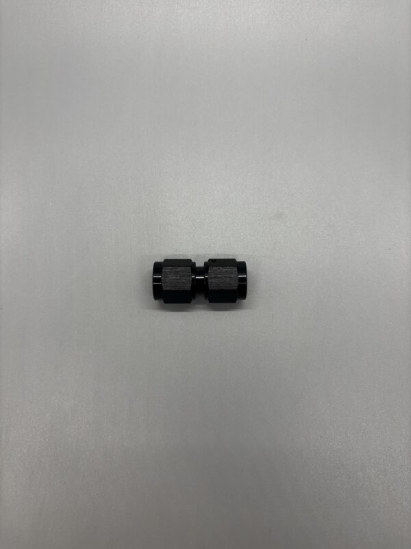 Close-up of a black 6 AN female to female adapter used in automotive fluid systems, placed on a plain surface.